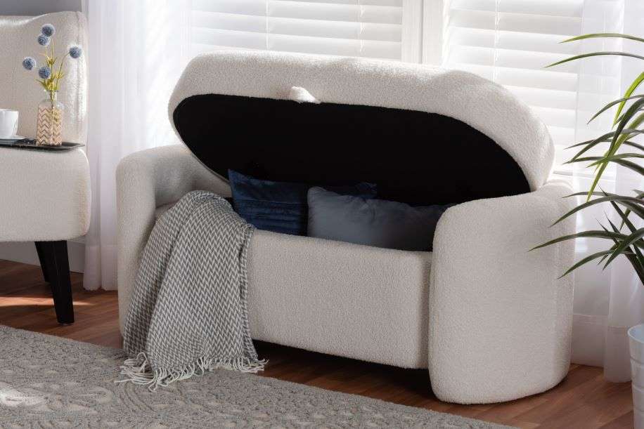White storage bench with a black interior, two blue pillows, and a gray blanket.
