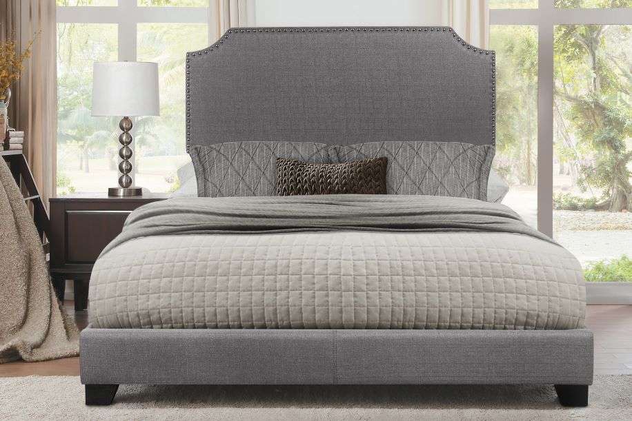 Gray upholstered bed with a tufted headboard and a patterned quilt.