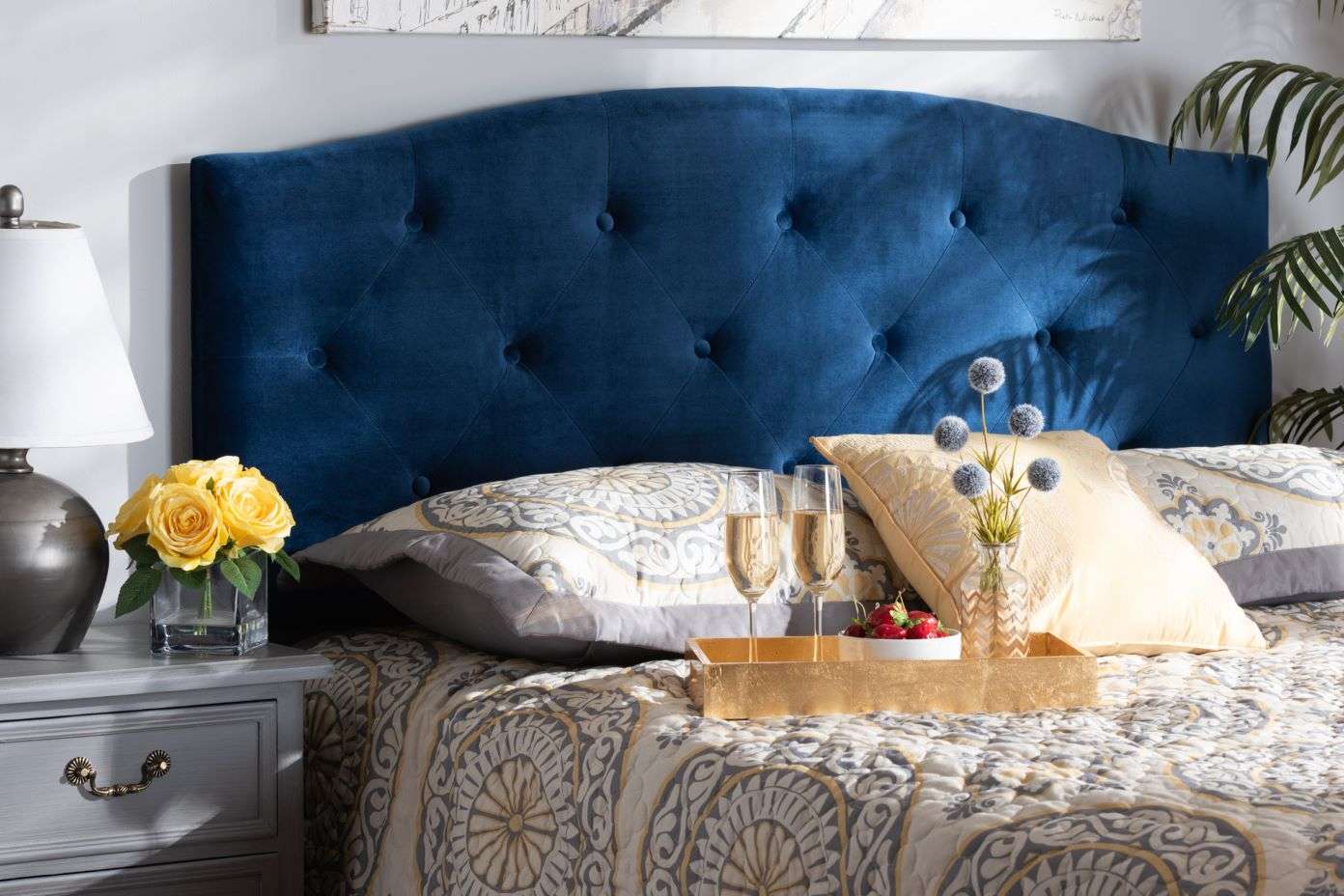 Blue velvet tufted headboard with pillows, champagne, and flowers.
