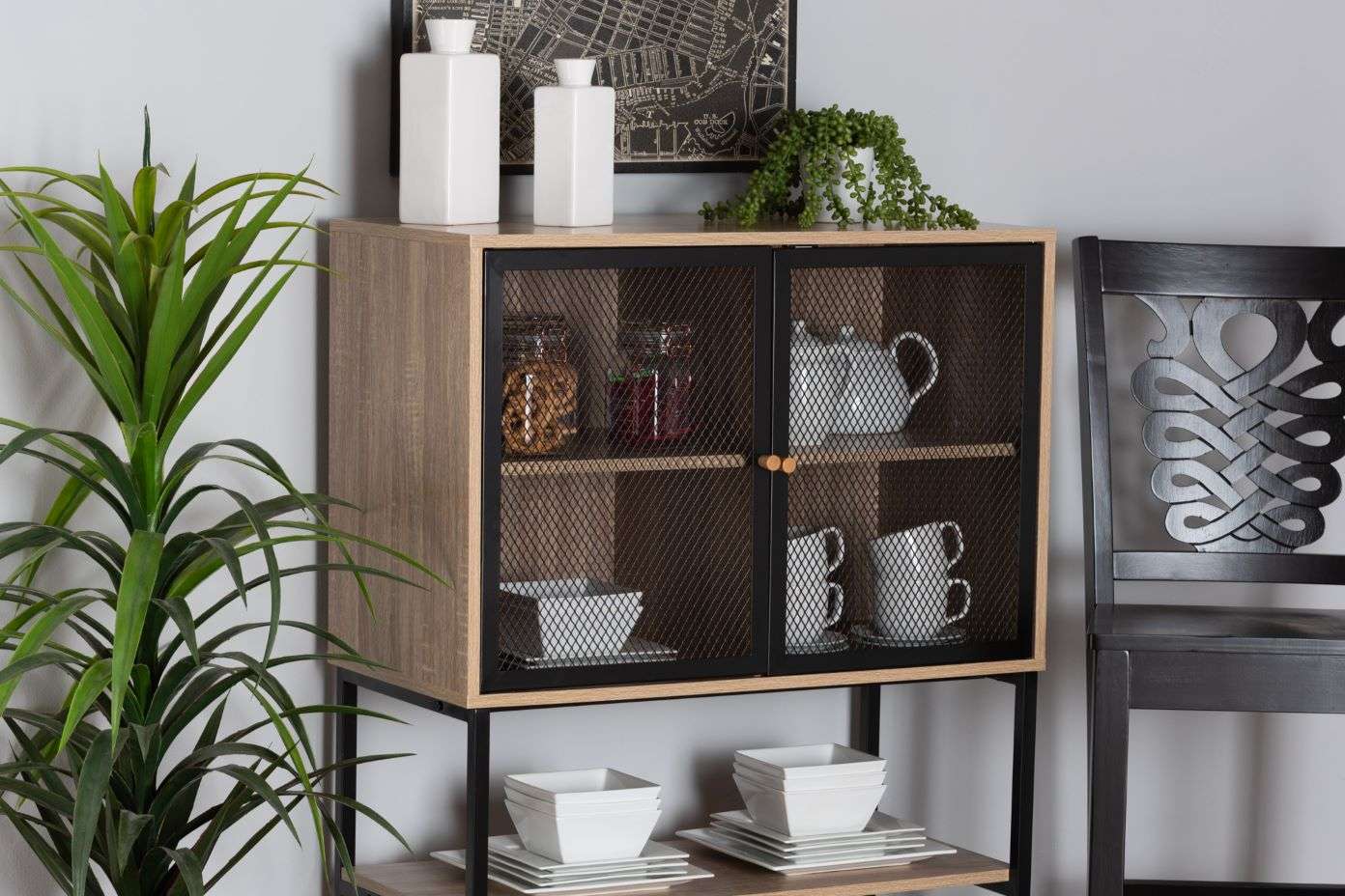Wooden cabinet with mesh doors, holding dishes and jars. A plant and chair are nearby.
