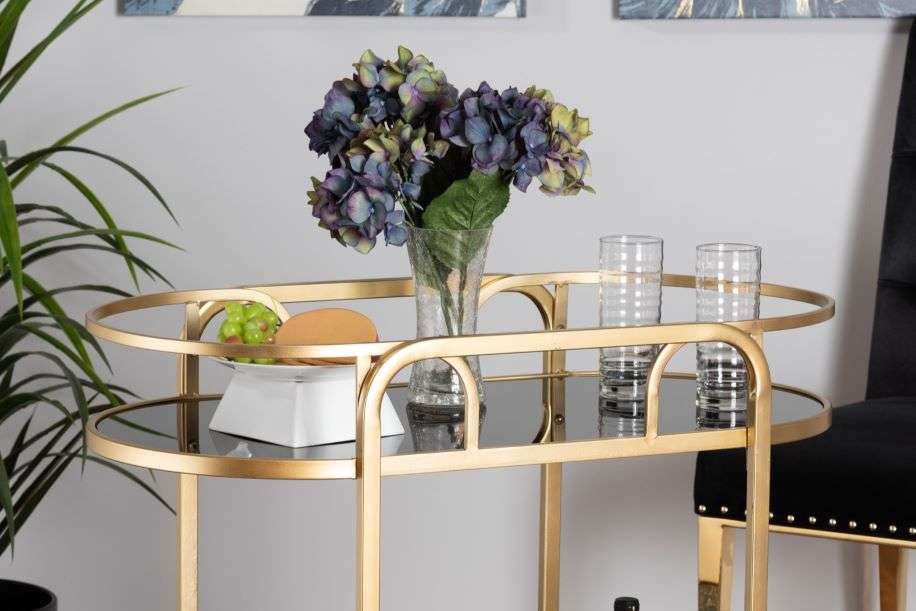 Gold bar cart with flowers, glasses, and snacks.
