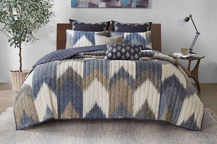 A bed with a blue, white, and brown patterned quilt, pillows, and a wooden headboard.