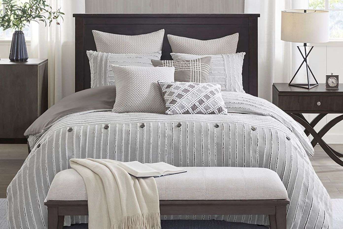 Bedroom with a dark wooden bed frame, gray bedding, and a bench at the foot of the bed.