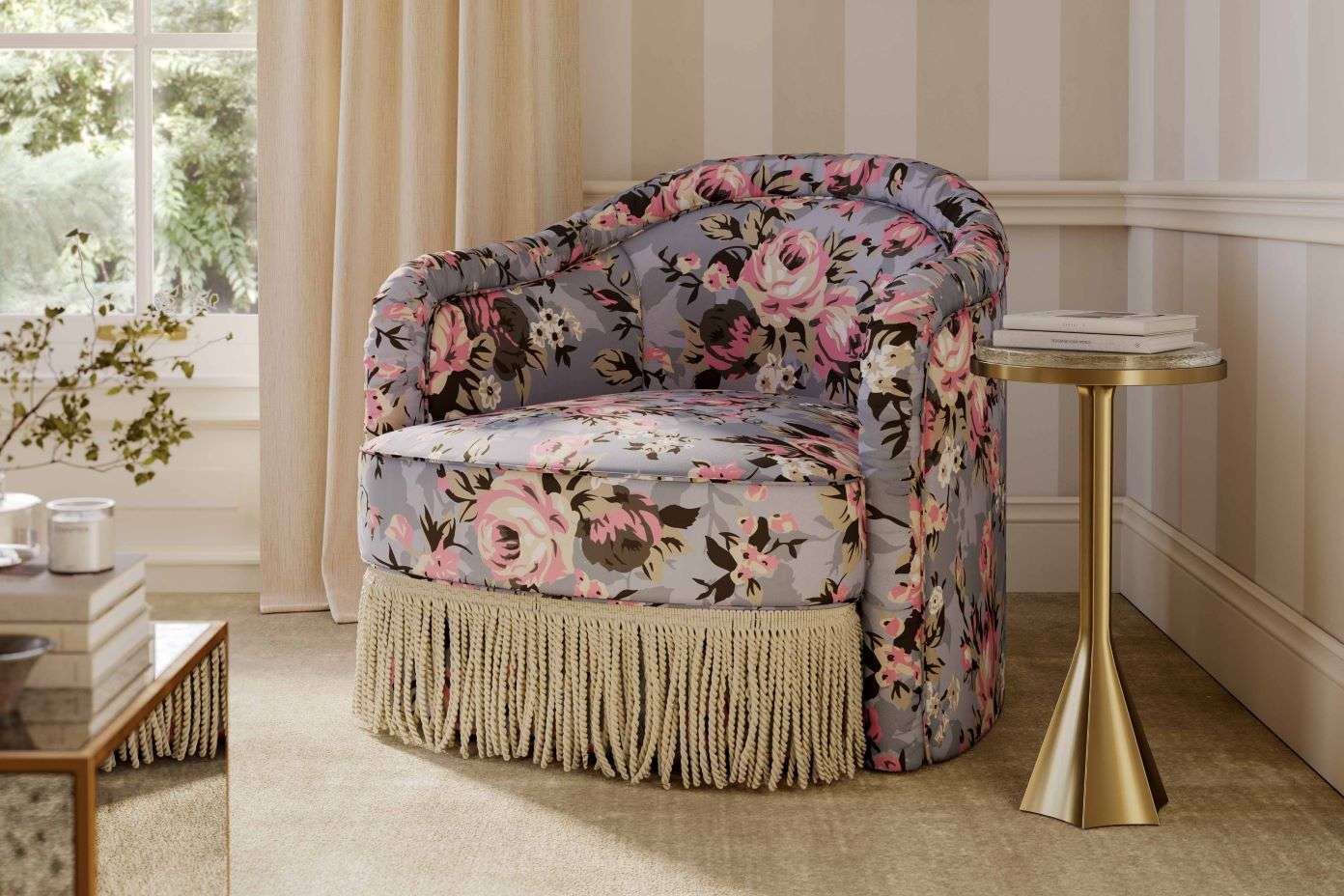 Floral patterned armchair with fringe. A small side table with books is next to the chair.