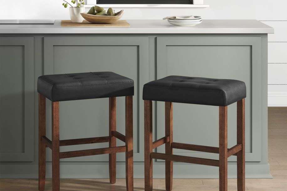 Two black leather bar stools with wooden legs.
