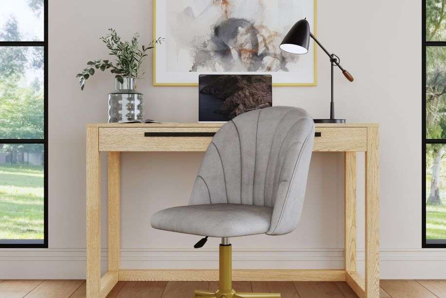 A light wood desk with a gray chair, a black lamp, and a painting.
