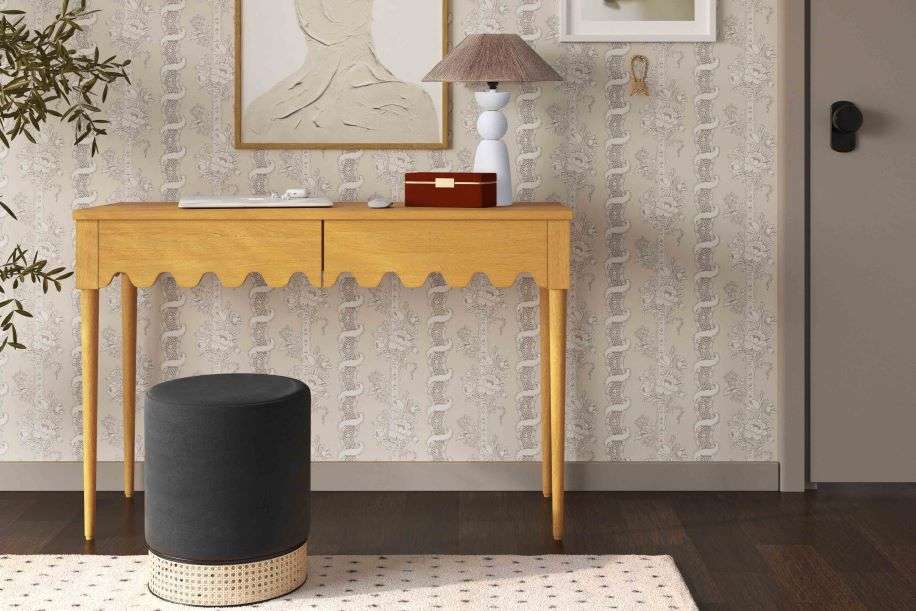 Yellow desk with scalloped edge, black stool, and patterned wallpaper.
