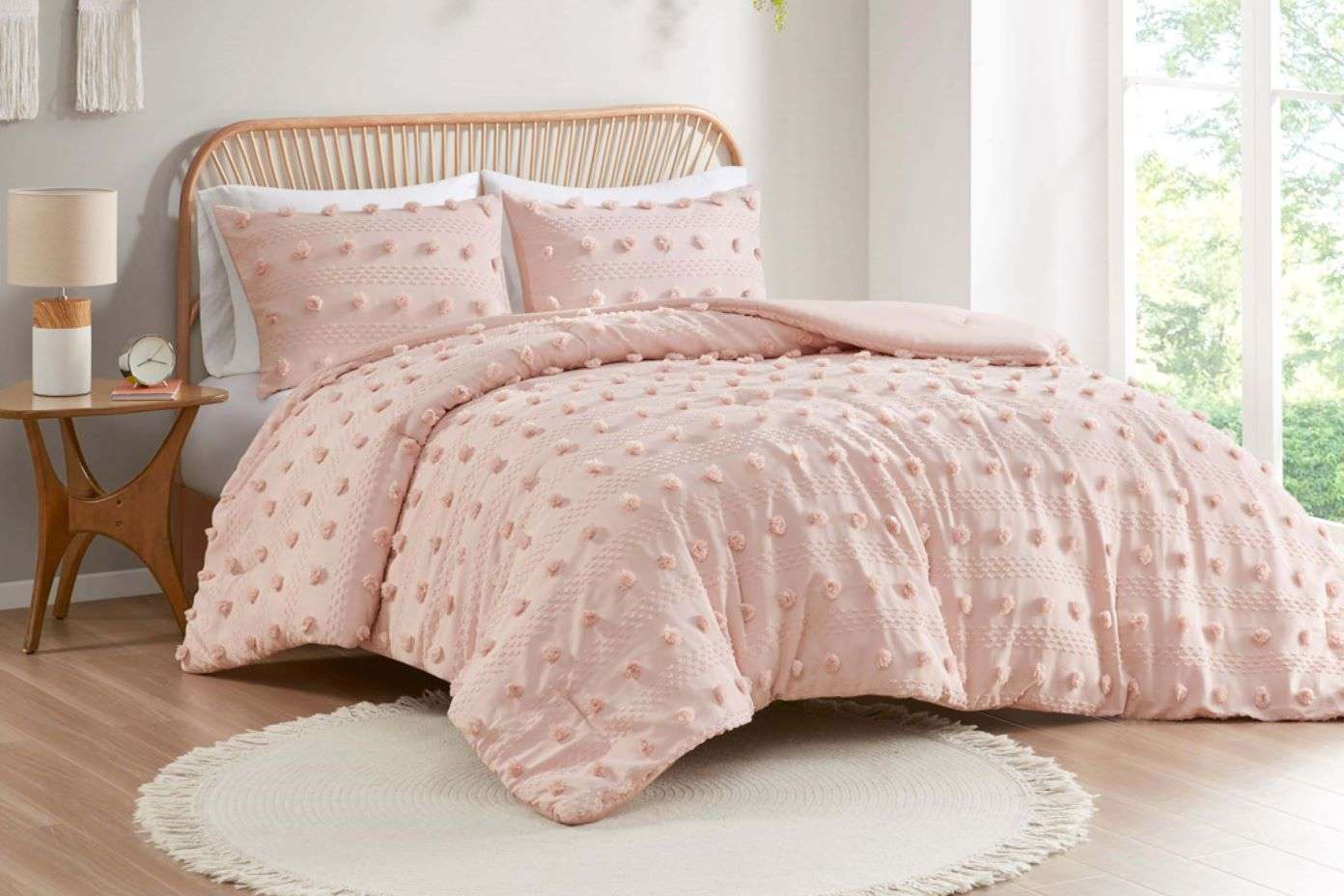 Pink tufted comforter set on a bed with a round rug.
