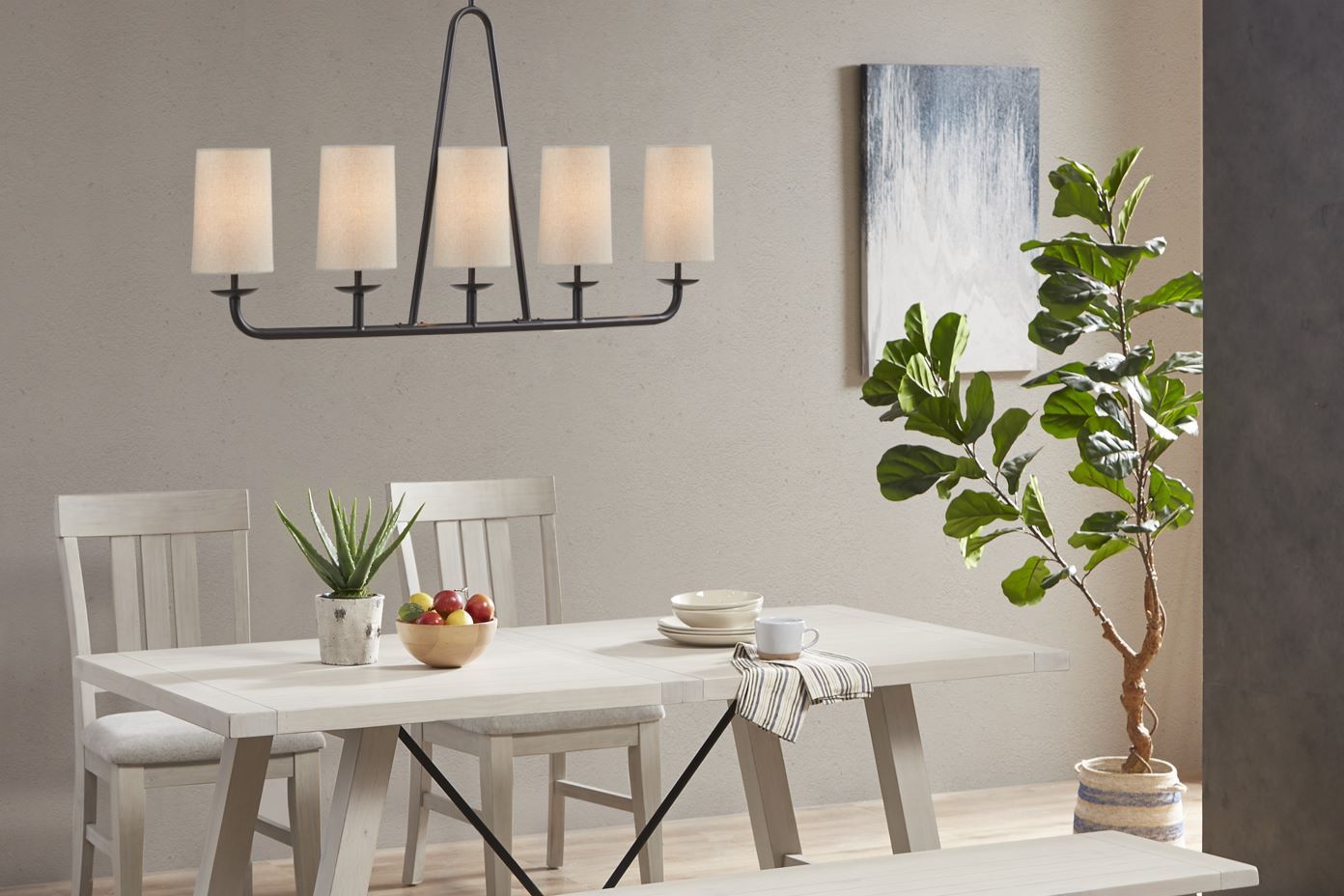 A dining room with a white table, chairs, and a chandelier. There is a plant in the corner.
