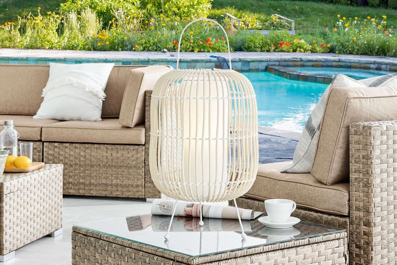 White wicker lantern on a glass-topped table next to a pool.