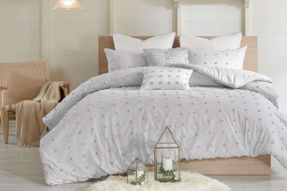 Bed with gray comforter and pillows, decorative lanterns, and a chair with a blanket.