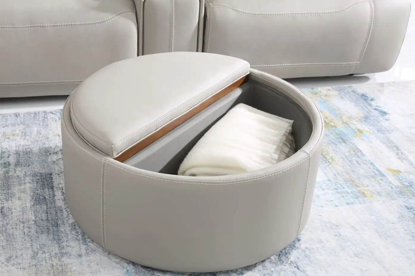 A gray leather ottoman with a blanket inside.