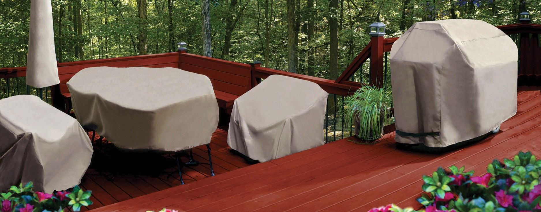 Outdoor furniture covered with beige protective covers on a wooden deck.
