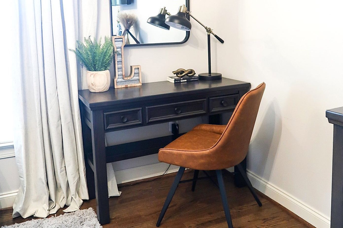 A dark wooden desk with a brown leather chair, a lamp, and a mirror.
