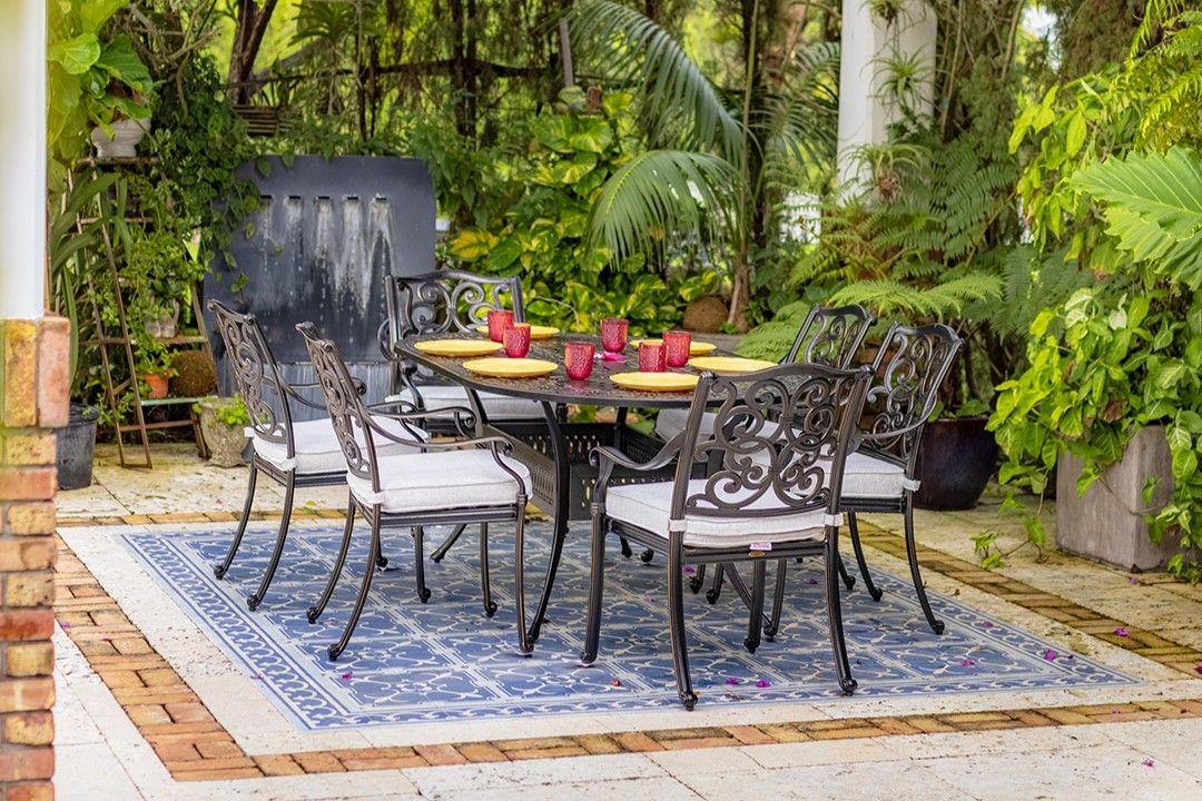 A patio dining set with a table, chairs, and place settings on a blue patterned rug.
