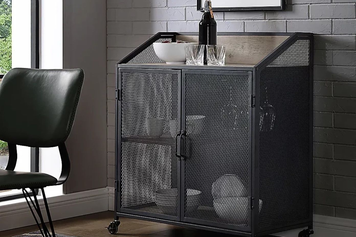 Black metal bar cabinet with mesh doors, a bottle, glasses, and a bowl on top.
