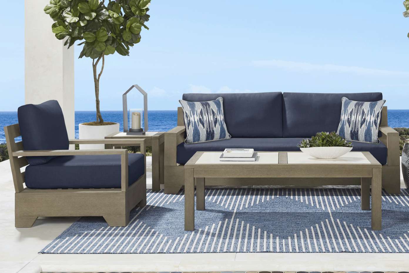 Outdoor furniture set with a sofa, armchair, and coffee table on a blue rug.

