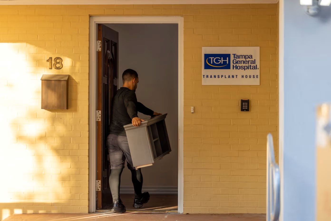 Tampa General Hospital Transplant House. A person carrying a gray cabinet through a doorway.
