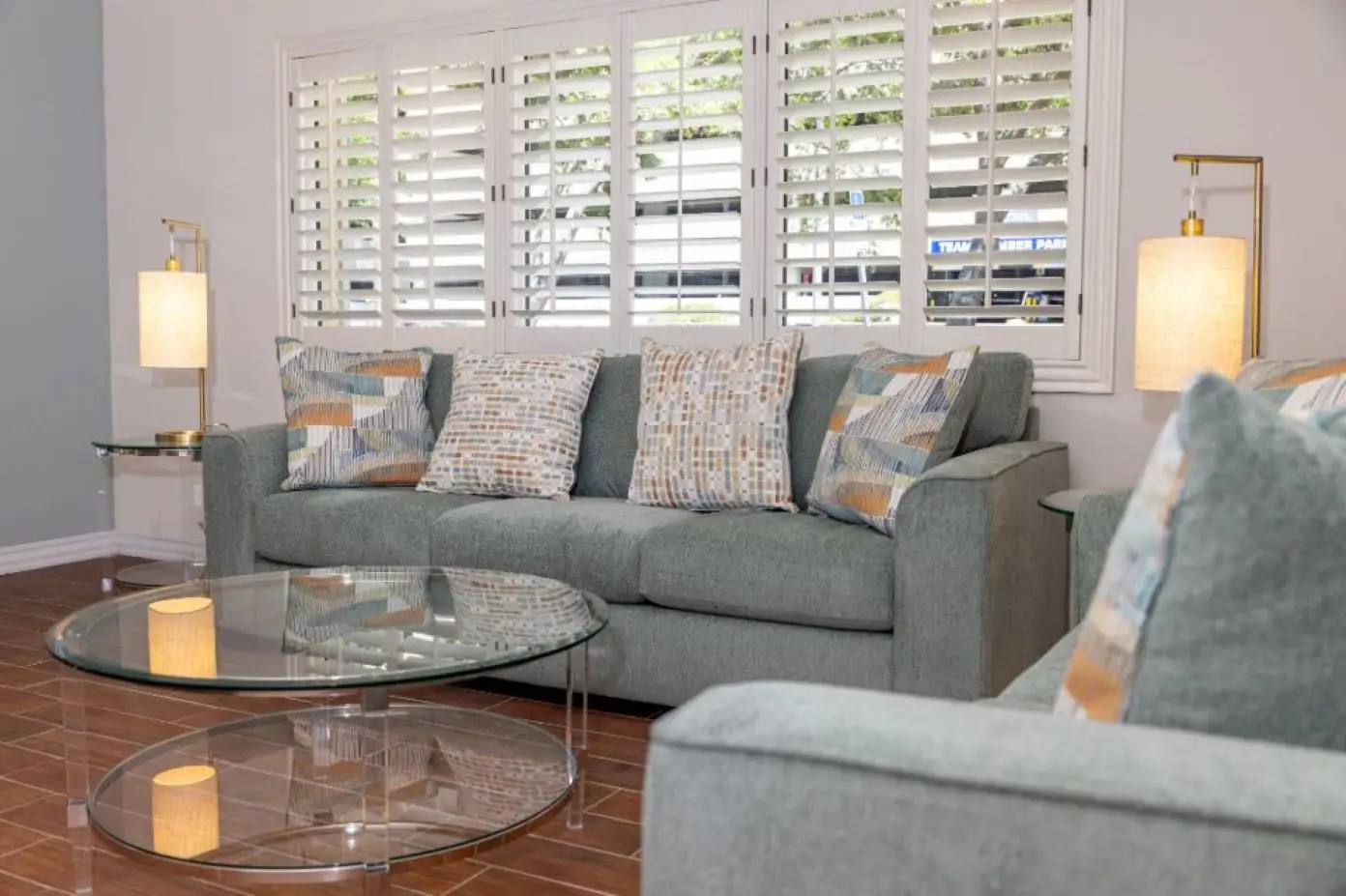 A living room with a green sofa, glass coffee table, and lamps.

