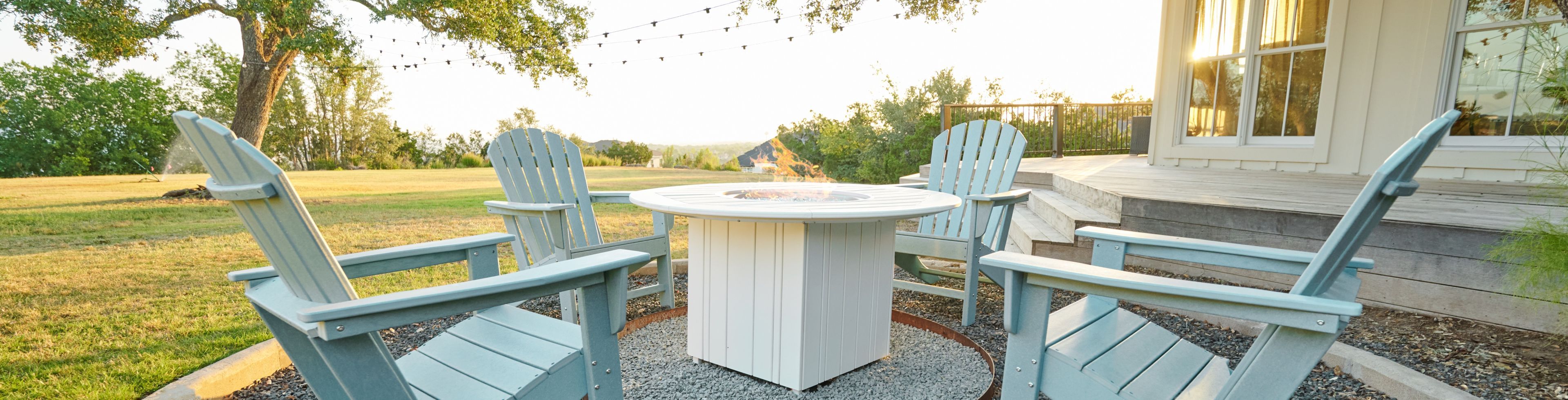Four blue Adirondack chairs around a white fire pit on a gravel patio.