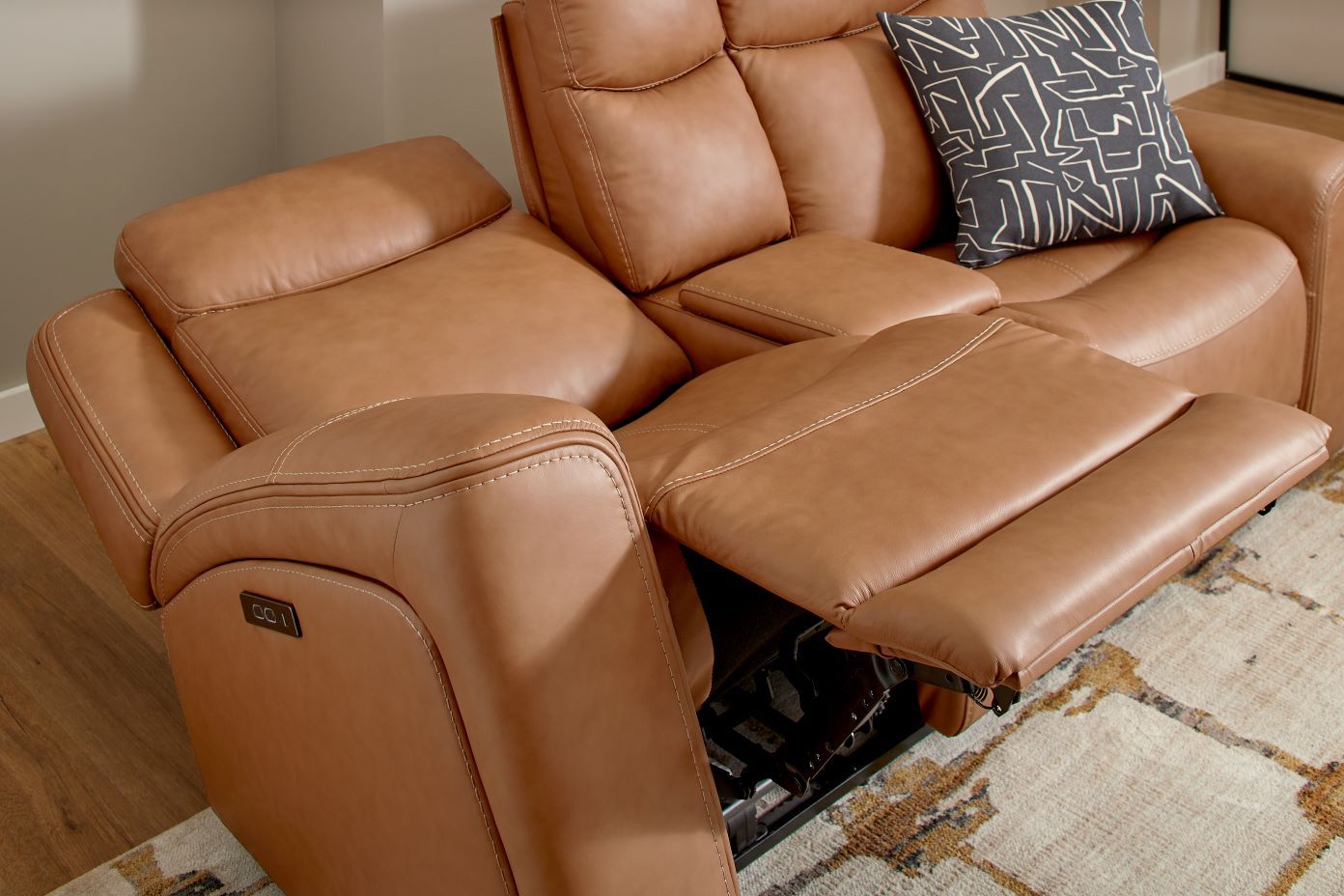 Brown leather reclining sofa with a patterned pillow.
