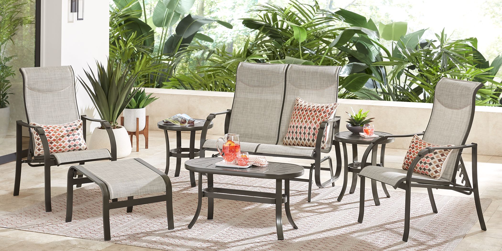 Photo of bronze outdoor sling loveseat and sling chairs with pillows and a coordinating ottoman